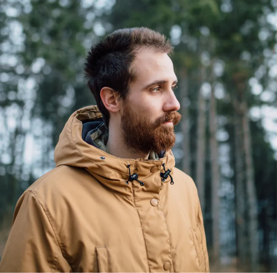 A man in a jacket looking off in the distance with trees behind him